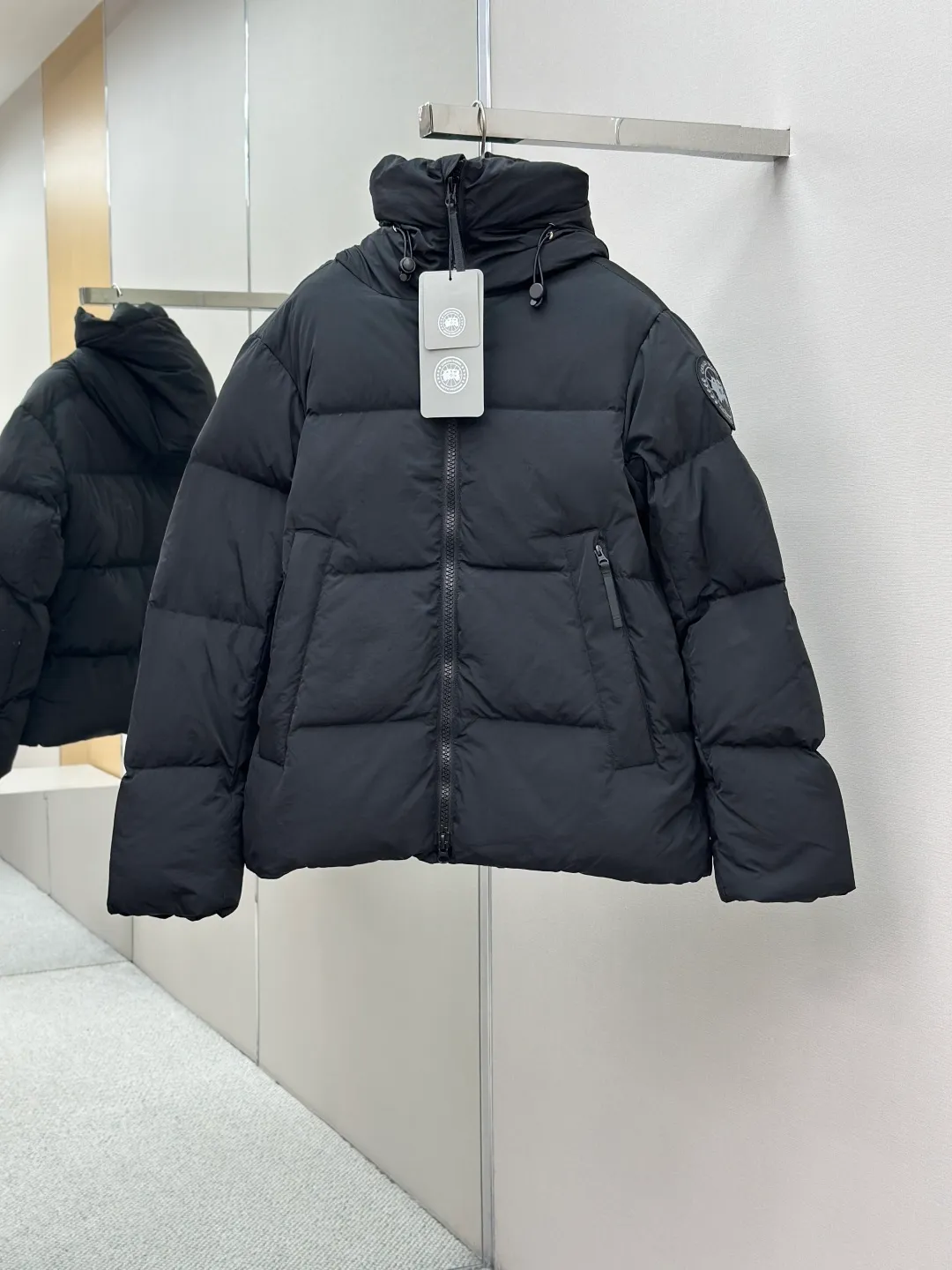 P1010 Canada Goose Black Label Badge Hooded Down Jacket (khaki) The high-quality filling is made of 90 national standard high-quality white duck down, selected high-loft velvet, weighing 240g, light and warm, with excellent temperature locking performance and good resilience. The fabric is woven with 400T high-count yarn. After special water-repellent treatment, the surface forms a lotus leaf effect - raindrops will slide down like beads, and snow particles will fall off when touched. The tear resistance reaches 200N (approximately 20kg load-bearing), the light gray matte texture breaks the stereotype of "outdoor clothing = hardcore", and the soft luster presents a high-end matte effect under urban neon lights, seamlessly switching scenes from ski resorts to CBD office buildings. The ribbon is woven with polyester as the base, and the brand letters are decorated on the ribbon through high-precision computer embroidery. The edges of the pattern are clear, the stitches are fine and even, and multiple layers of embroidery thread are stacked to enhance the three-dimensional effect. Precision thread reinforcement prevents linting and ensures the fluffy and resilient elasticity lasts as new. The embedded cuffs are three-dimensionally woven to form a "wavy" elastic structure, which forms natural folds when fitting the wrist, increasing the contact area with the skin, thus improving the windproof effect. At the same time, micro-velvet treatment is added to the inside of the cuffs, which feels like a second layer of skin and avoids friction on the skin from metal zippers or hard fabrics. Size:S-M-L-XL